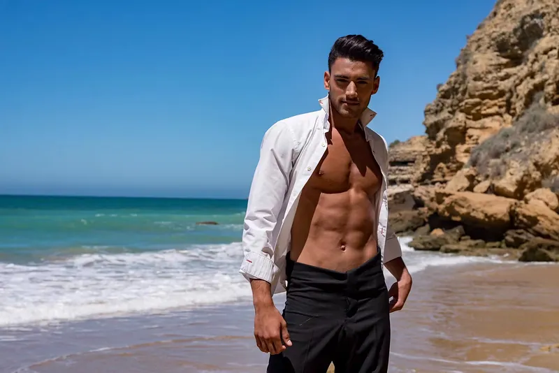 Modelo masculino con camisa blanca abierta en una cala de acantilados