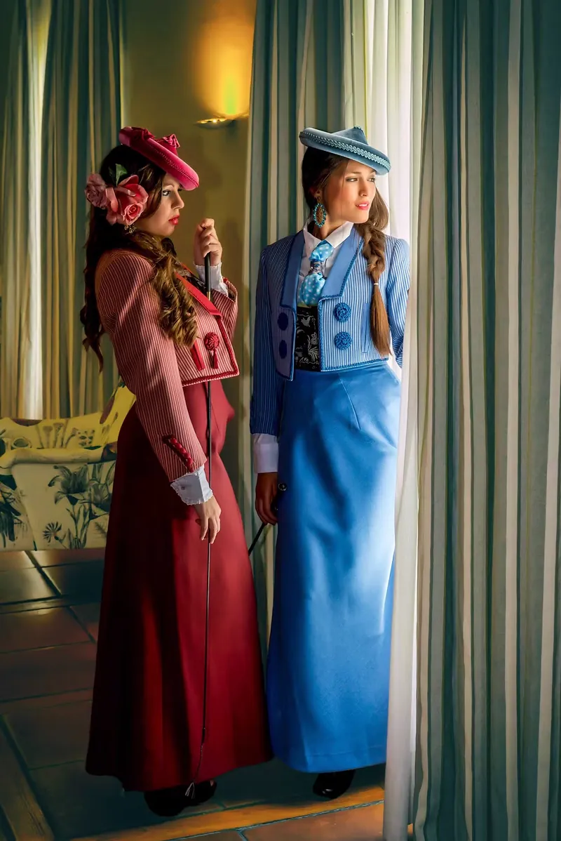 Dos modelos con trajes de época, en rosa y azul, posando en un portal