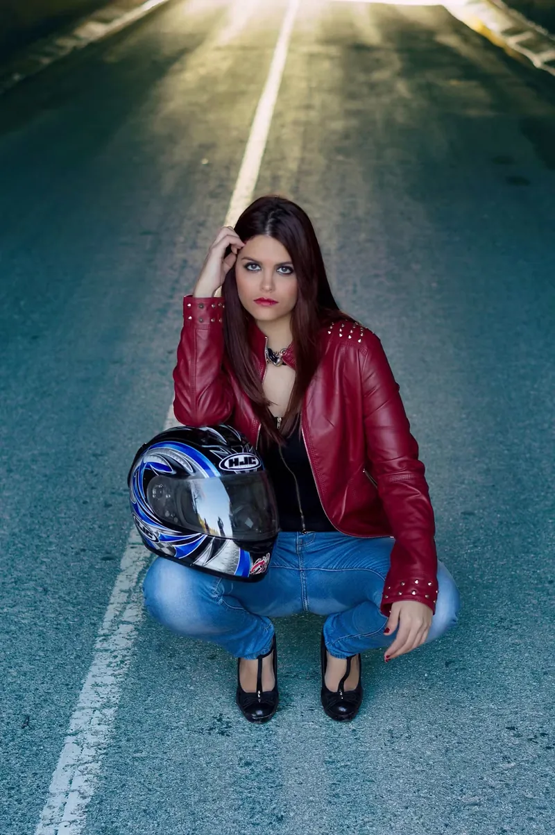 Modelo con chaqueta roja y casco de moto sentada en mitad de una carretera