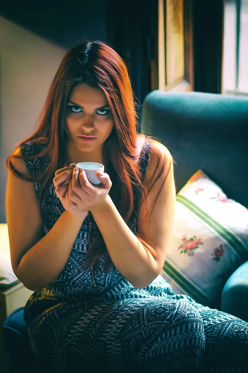 Retrato de interior: modelo con vestido verde sosteniendo una taza en un sofá