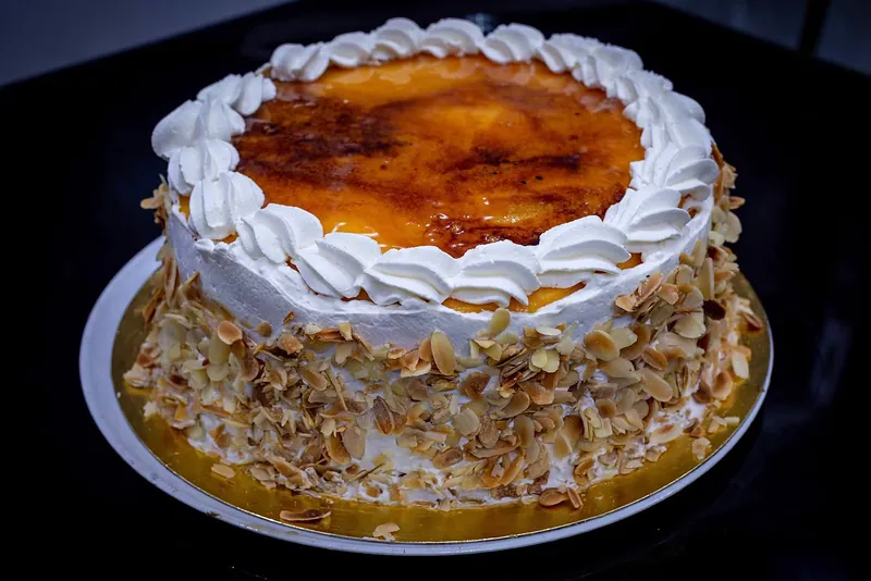 Tarta entera de nata y almendra con la superficie tostada, sobre fondo oscuro