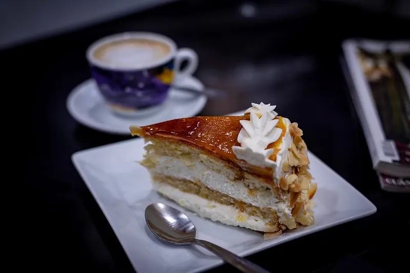 Ración de tarta con nata emplatada en blanco junto a una taza de café
