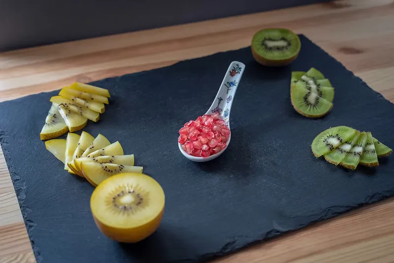 Emplatado sobre pizarra con kiwi verde y amarillo laminado y granos de granada