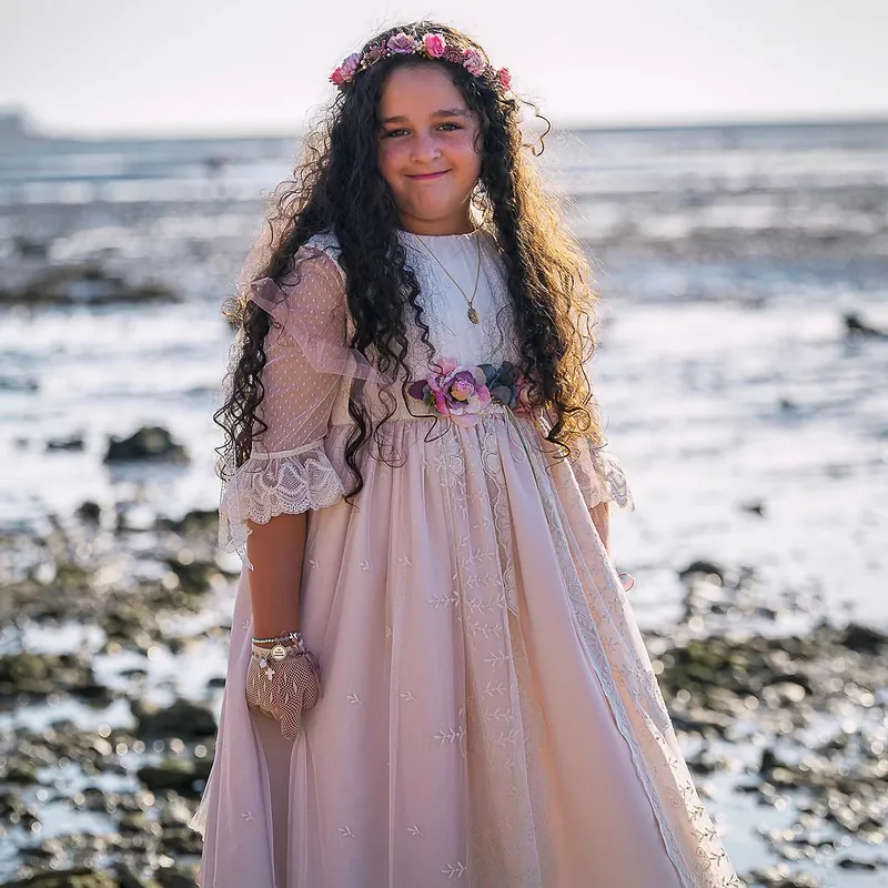 Niña de comunión posando en la orilla con la marea baja