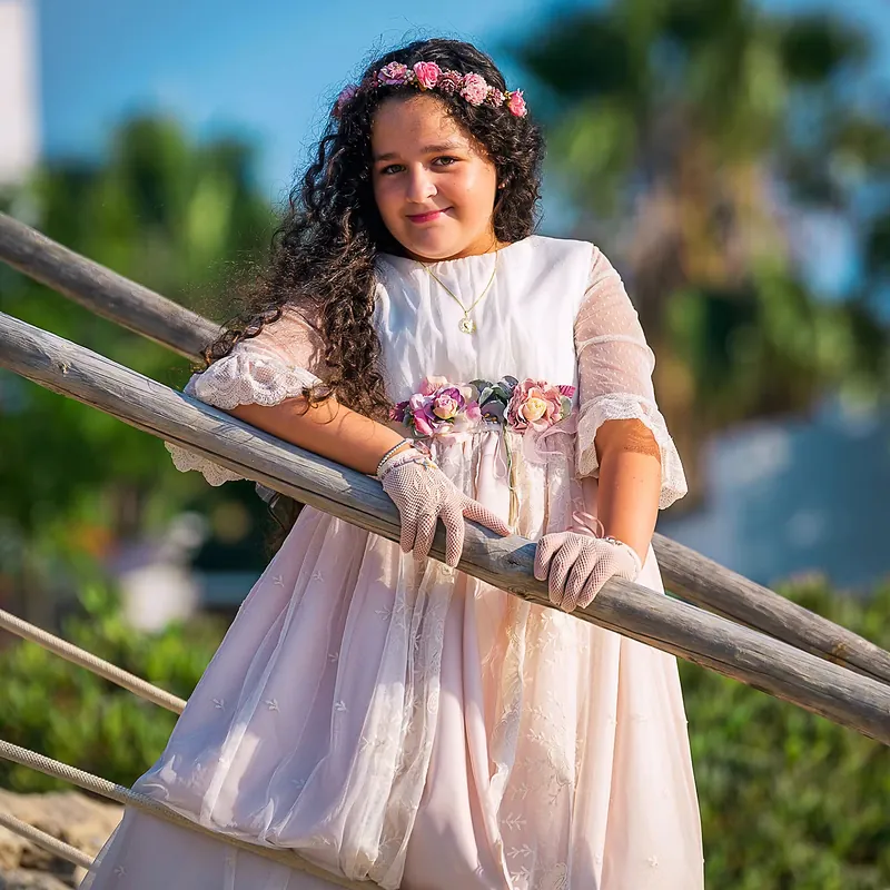 Retrato de niña de comunión con corona de flores apoyada en una barandilla