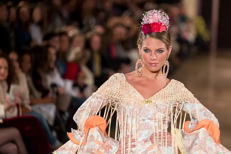 Modelo desfilando con traje de flamenca beige de flecos ante el público