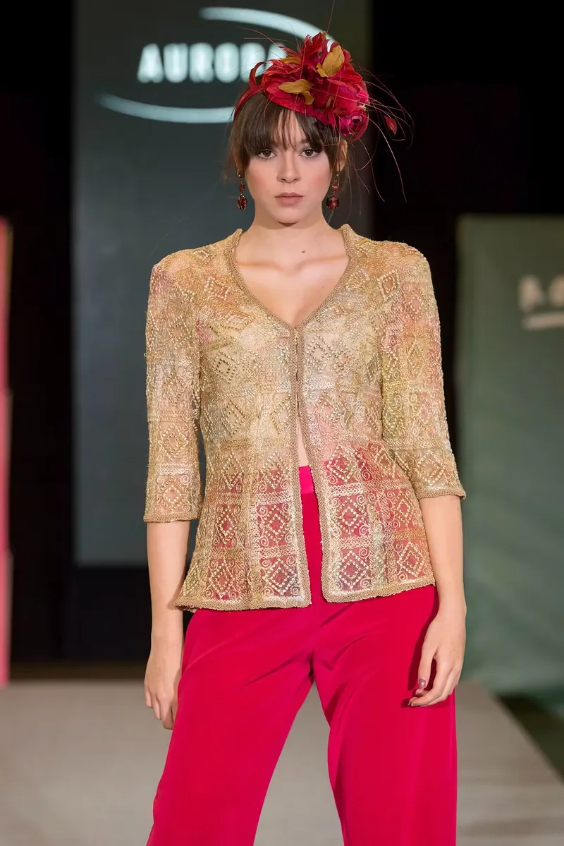 Modelo en pasarela con chaqueta de encaje dorado y pantalón rojo