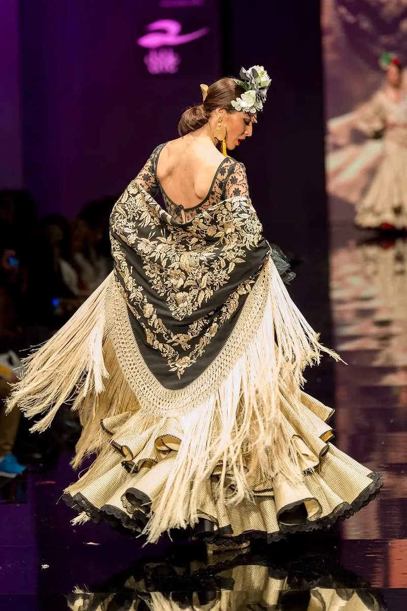 Modelo de espaldas girando con un mantón de flecos en la pasarela flamenca