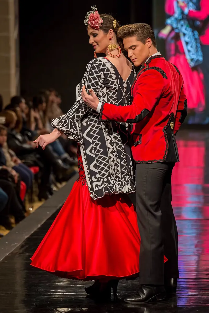 Pareja de modelos desfilando con trajes flamencos en rojo y negro