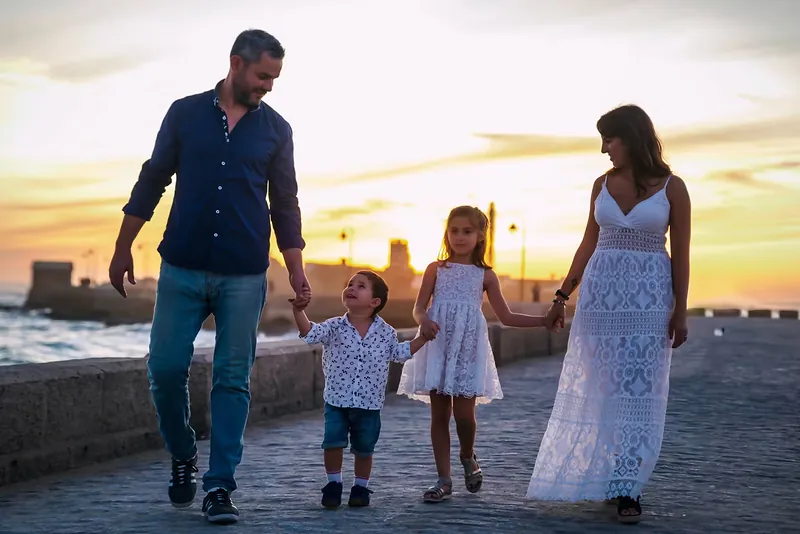 Familia con dos niños paseando de la mano por el paseo marítimo al atardecer