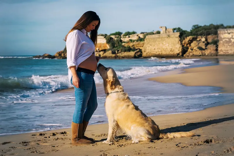 Embarazada acariciando a su perro en la orilla, con los acantilados de fondo