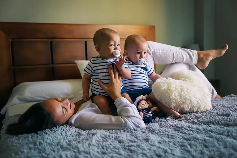 Sesión de recién nacidos: madre con sus bebés gemelos sobre la cama