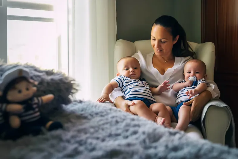 Madre con sus dos bebés gemelos en un sillón junto a la ventana