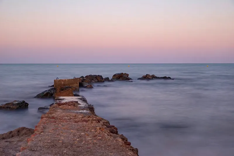 Espigón de piedra adentrándose en el mar, fotografiado en larga exposición al atardecer
