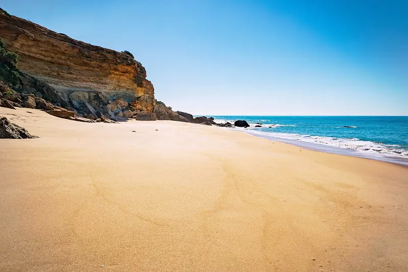 Cala de arena dorada al pie de un acantilado con el mar turquesa