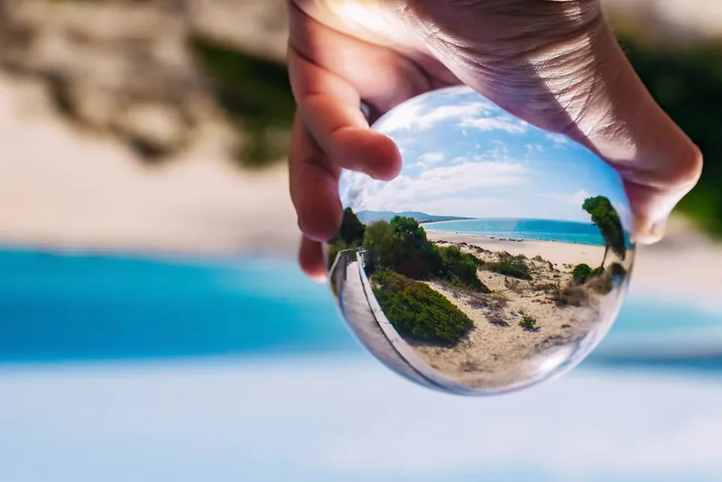 Mano sosteniendo una esfera de cristal que invierte el paisaje de la playa
