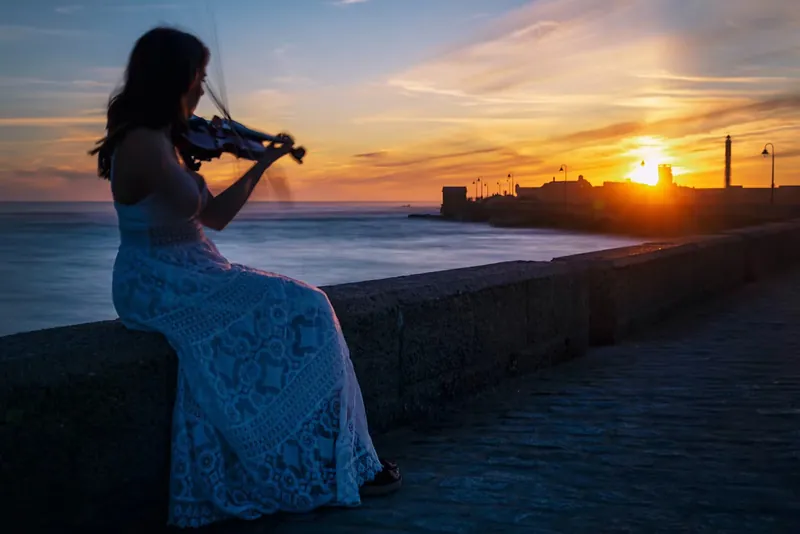 Violinista tocando de espaldas sobre la muralla de Cádiz al atardecer