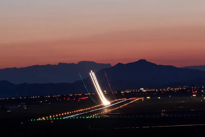 Larga exposición nocturna: estela de luz sobre la ciudad con la sierra al fondo